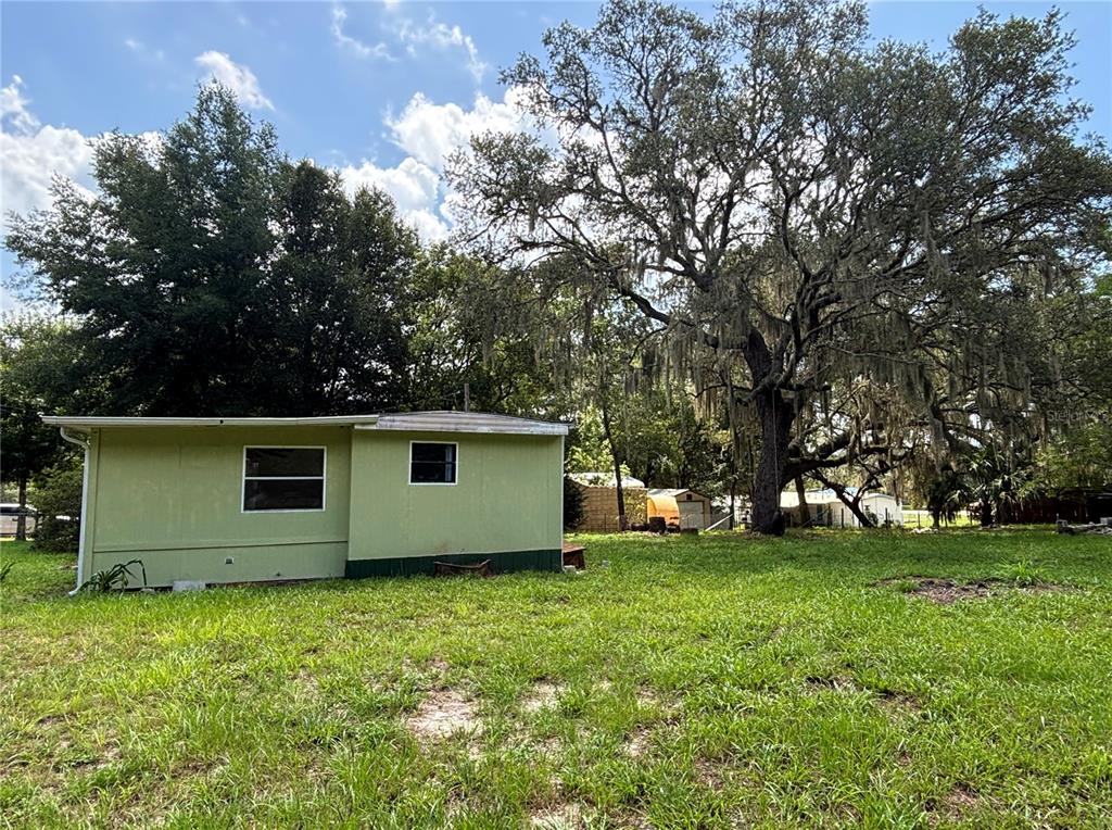 A light green exterior wall of a small house stands beside a large oak tree — 18274 SE 22ND PLACE, SILVER SPRINGS, FL
