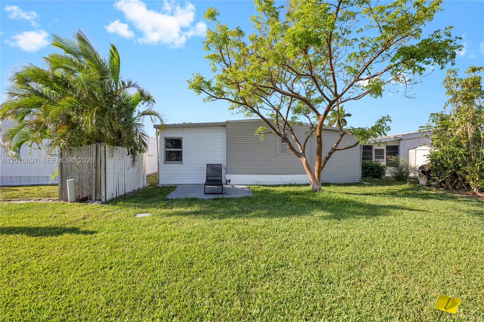 The exterior of a mobile home features a small concrete patio and a large tree — 2148 SW 52nd St, Dania Beach FL 33312, DANIA BEACH, FL