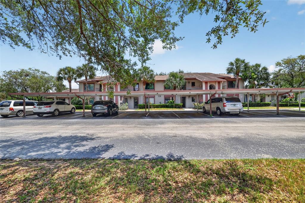 A two-story apartment building with covered parking spaces and several parked cars in front — 731 83RD AVENUE N UNIT 105, ST PETERSBURG, FL