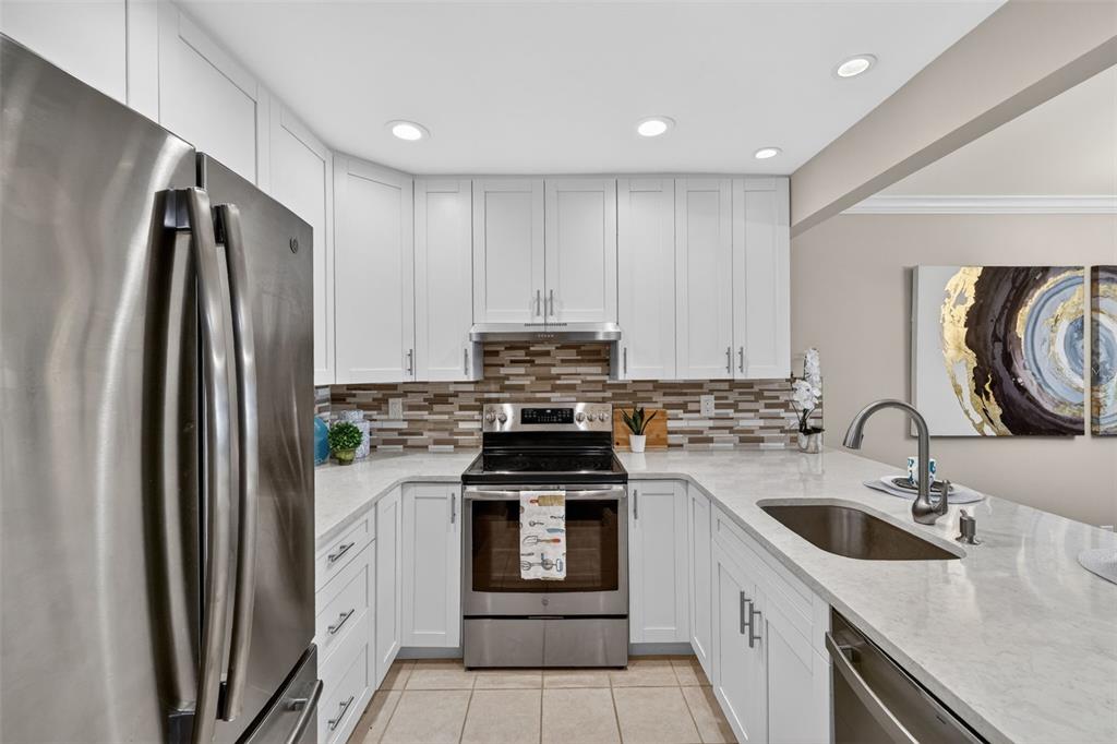 A modern kitchen features white cabinetry, stainless steel appliances, a tiled backsplash, and quartz countertops — 731 83RD AVENUE N UNIT 105, ST PETERSBURG, FL