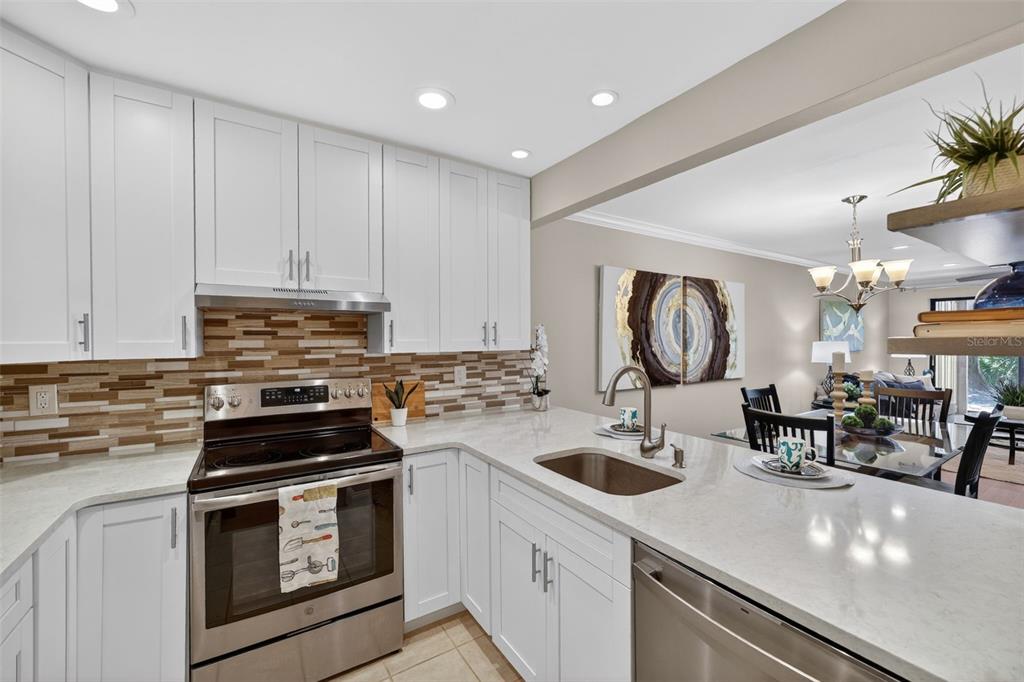 A kitchen with white cabinets, stainless steel appliances, a tiled backsplash, and quartz countertops — 731 83RD AVENUE N UNIT 105, ST PETERSBURG, FL
