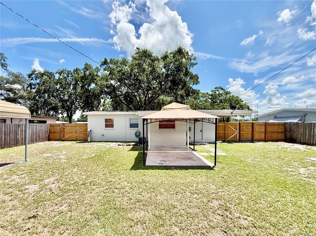 A backyard features a white house with a tan gazebo on a concrete patio — 7810 FELICE AVENUE, TAMPA, FL
