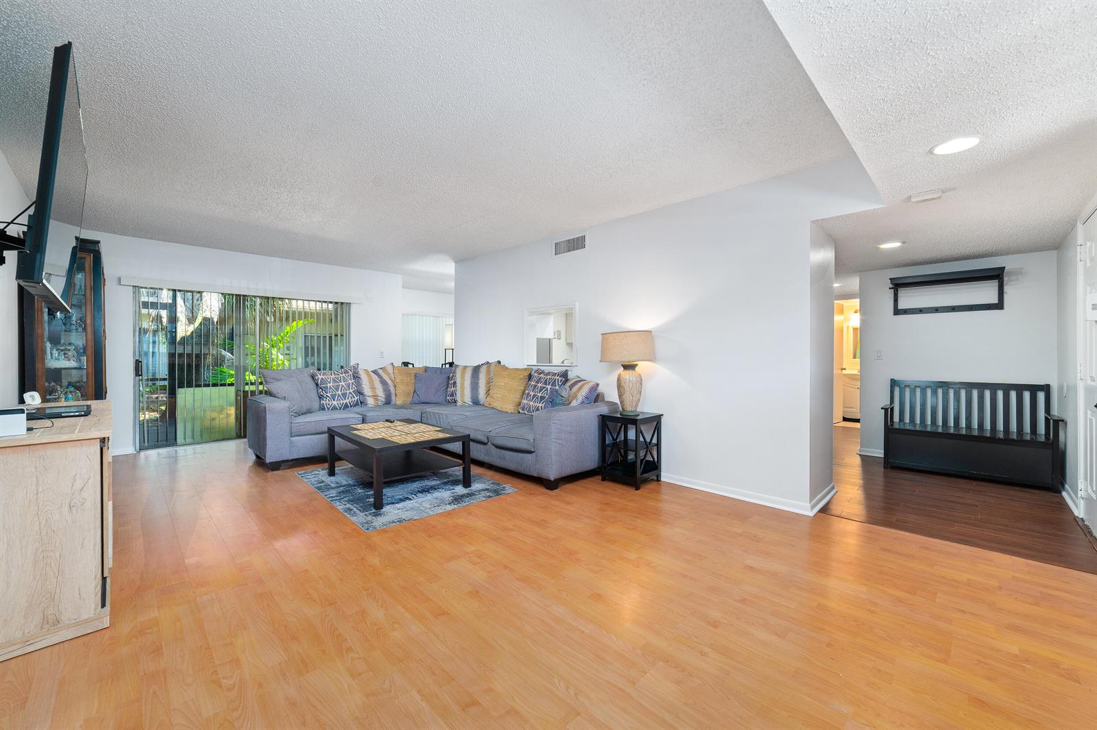 A living room features light wood flooring, a gray sectional sofa, and a black bench — 8968 W Sample Road # 101, Coral Springs FL 33065, CORAL SPRINGS, FL