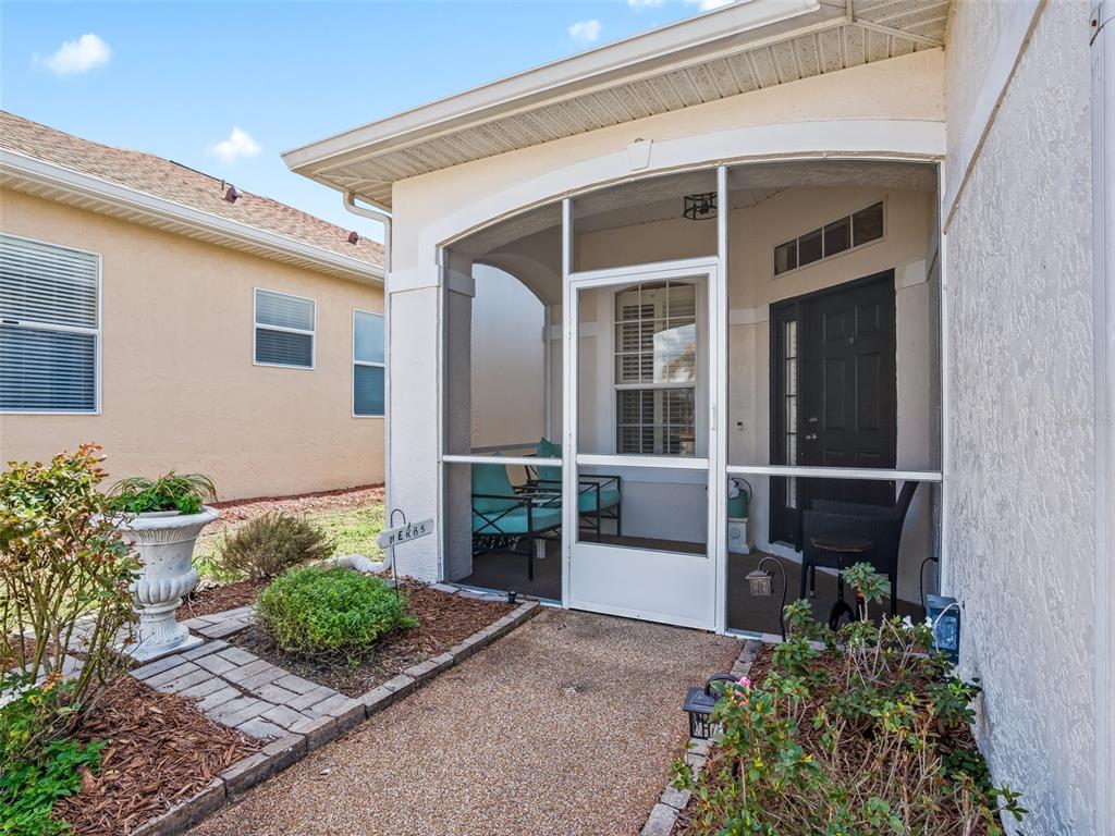 A screened-in front porch features a dark door, patio furniture, and a paved walkway — 11900 SE 178TH STREET, SUMMERFIELD, FL