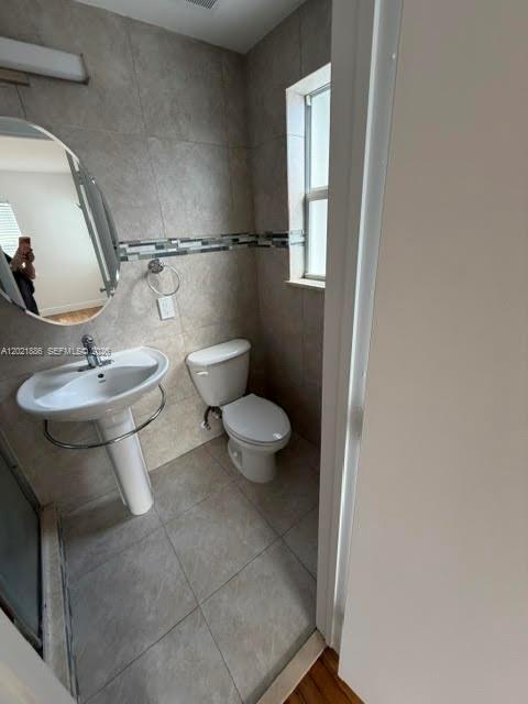 A bathroom features a pedestal sink, a toilet, and a mirror against tiled walls — 3311 S Le Jeune Rd # 2, Coral Gables FL 33134, CORAL GABLES, FL