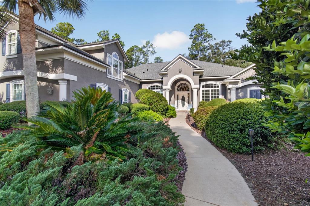 A concrete walkway leads to the front entrance of a gray house with arched windows — 1326 SW 90TH STREET, GAINESVILLE, FL
