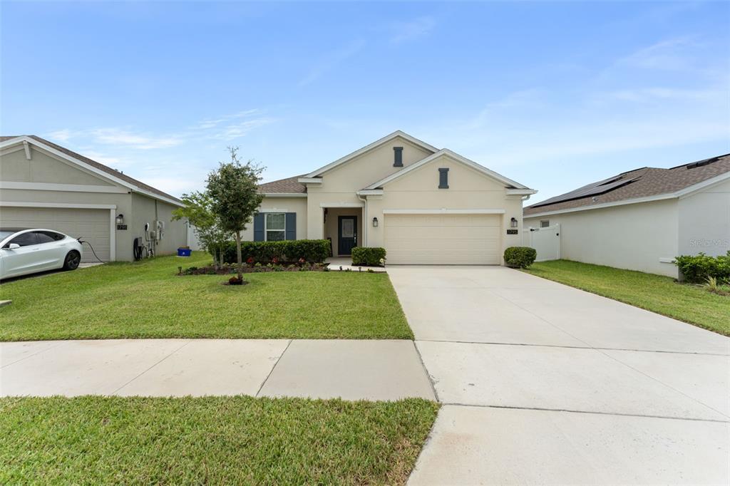 A single-story suburban house features a beige stucco exterior, a two-car garage, and a driveway — 1795 ROSS HAMMOCK AVENUE, GROVELAND, FL
