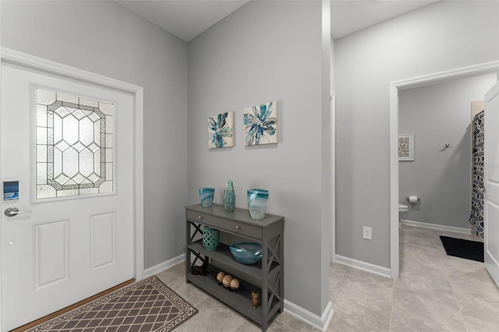 An entryway features a gray console table, two floral wall canvases, and a tiled floor — 1795 ROSS HAMMOCK AVENUE, GROVELAND, FL
