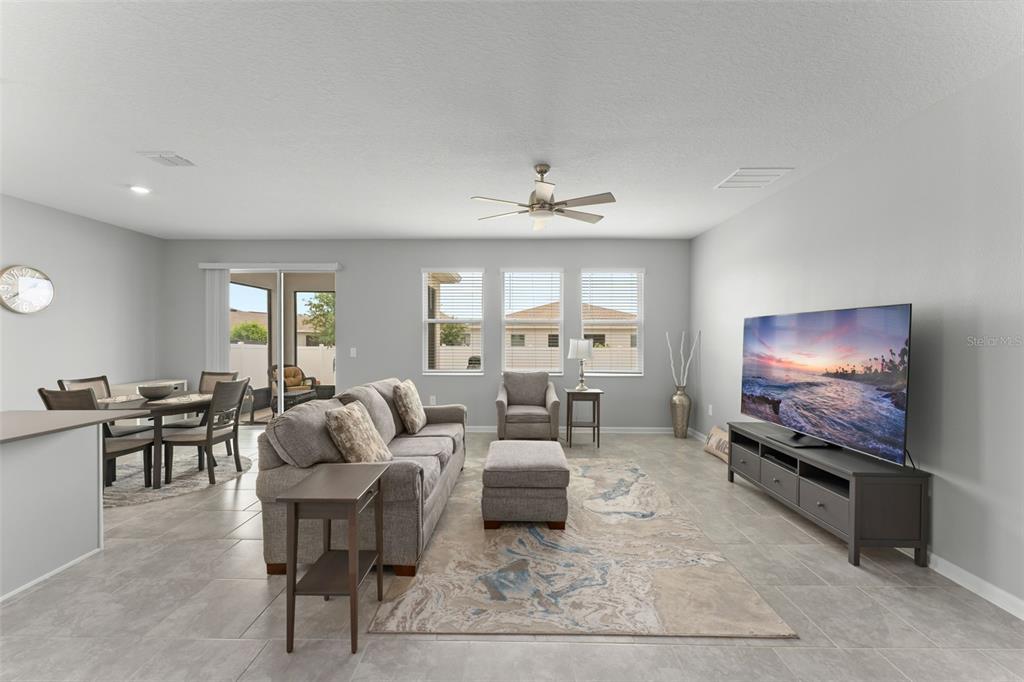 A living room features gray tile flooring, a gray sofa, a television, and a dining area — 1795 ROSS HAMMOCK AVENUE, GROVELAND, FL