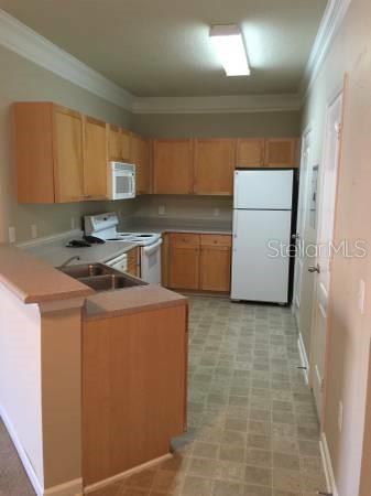 A kitchen features light wood cabinets, white appliances, a double sink, and tiled flooring — 19914 VILLA CREEK DRIVE UNIT 203, ORLANDO, FL