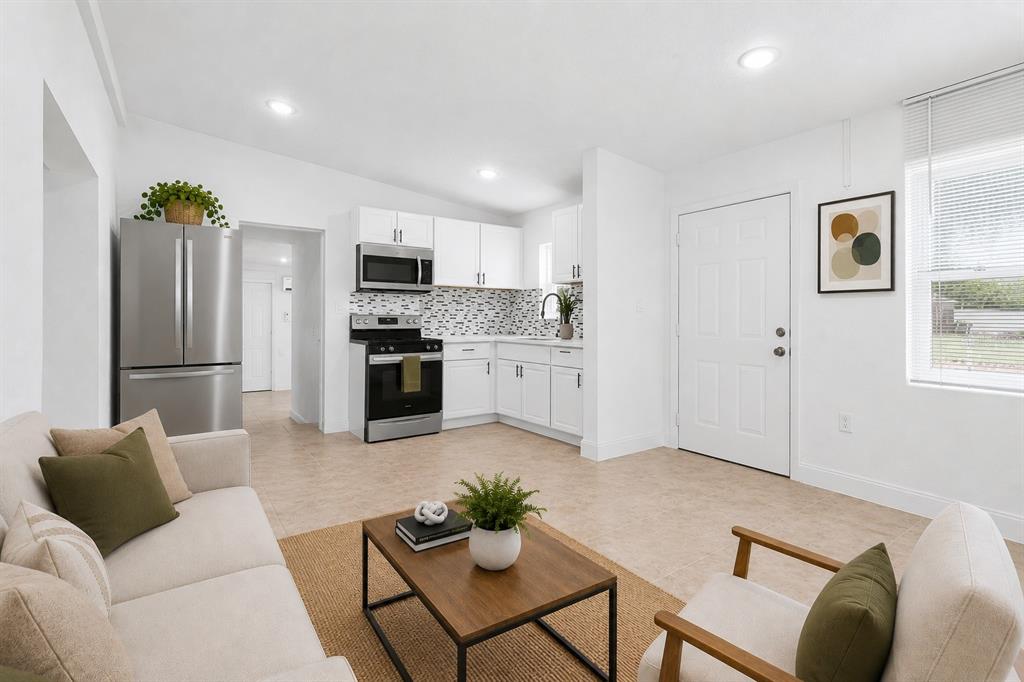A bright open-concept living room and kitchen featuring white cabinets, stainless appliances, and tile flooring — 918 FERNDELL ROAD, ORLANDO, FL