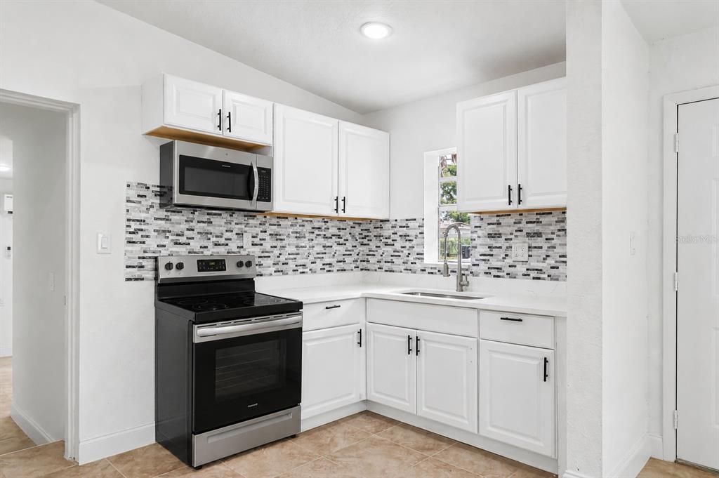 A kitchen features white cabinets, a black stove, a stainless microwave, and a mosaic backsplash — 918 FERNDELL ROAD, ORLANDO, FL