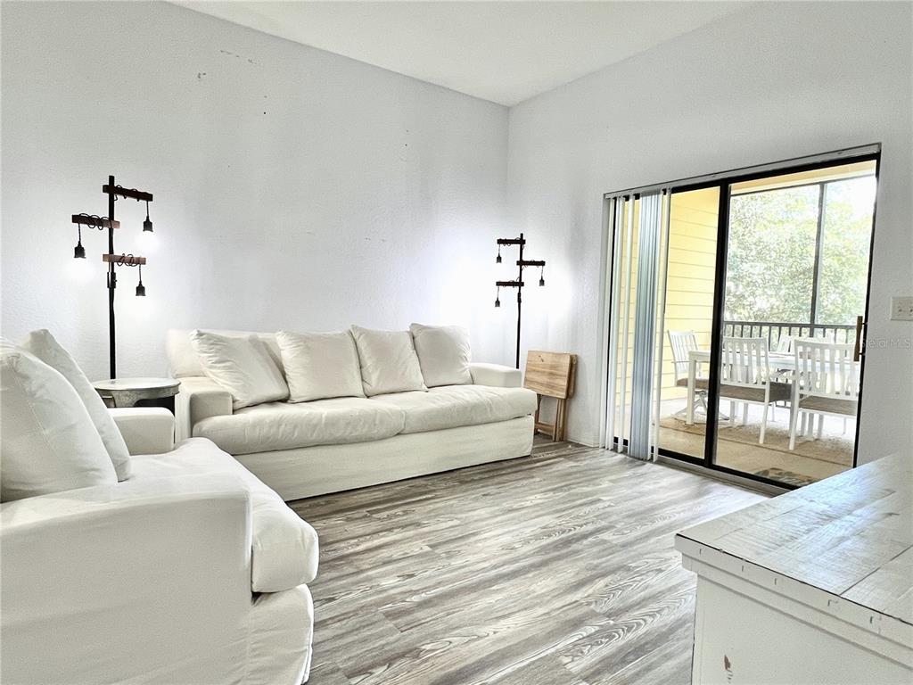 A living room features white sofas, two floor lamps, and sliding doors leading to a balcony — 9055 TREASURE TROVE LANE UNIT 207, KISSIMMEE, FL