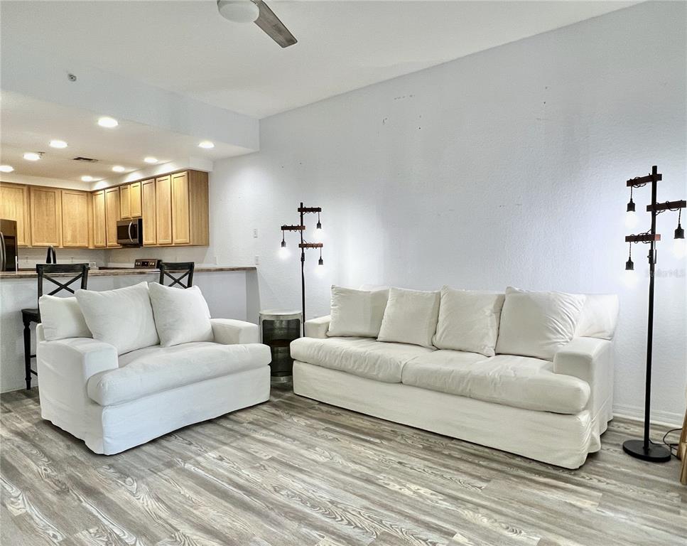 A living room with white slipcovered furniture, wood-look flooring, and two industrial-style floor lamps — 9055 TREASURE TROVE LANE UNIT 207, KISSIMMEE, FL