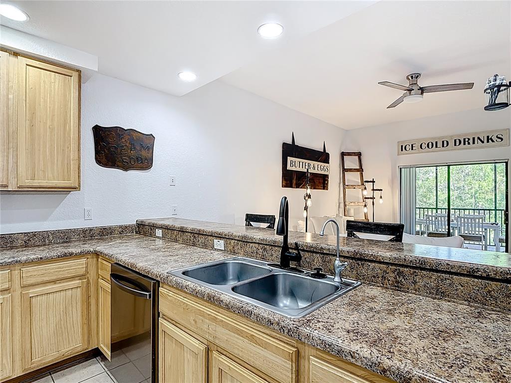 A kitchen features light wood cabinets, granite countertops, a double sink, and a breakfast bar — 9055 TREASURE TROVE LANE UNIT 207, KISSIMMEE, FL