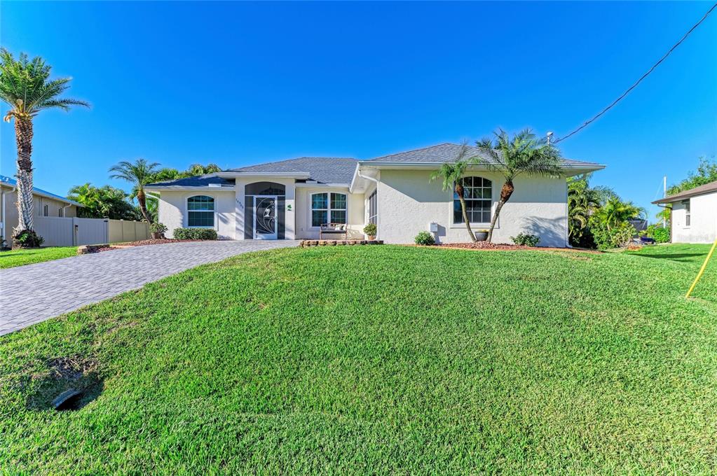 A single-story house with a paved driveway, green lawn, and palm trees under a blue sky — 14968 LYNEBURG AVENUE, PORT CHARLOTTE, FL