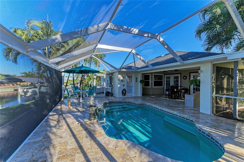 A screened-in pool patio features stone pavers, a small pool, and a canal view — 14968 LYNEBURG AVENUE, PORT CHARLOTTE, FL