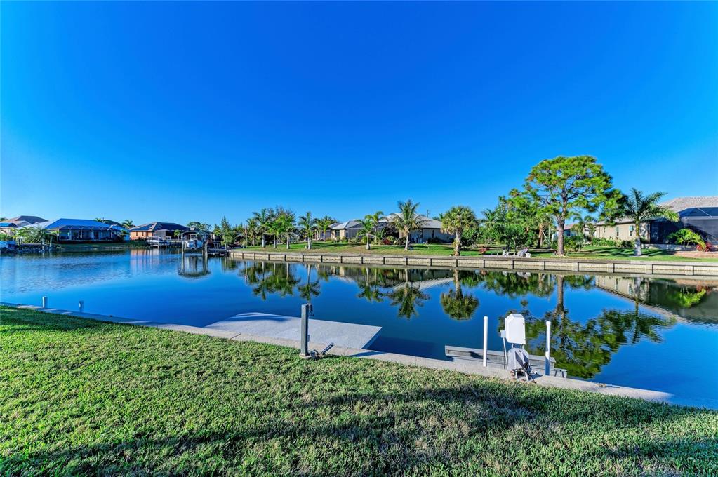 A canal view shows a grassy lawn, a concrete boat dock, and waterfront houses — 14968 LYNEBURG AVENUE, PORT CHARLOTTE, FL