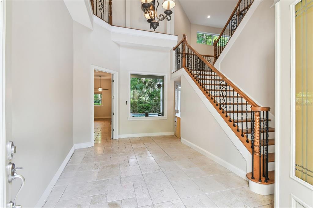 A bright foyer features stone tile flooring, a wooden staircase with iron railings, and a chandelier — 755 CRANES COURT, MAITLAND, FL