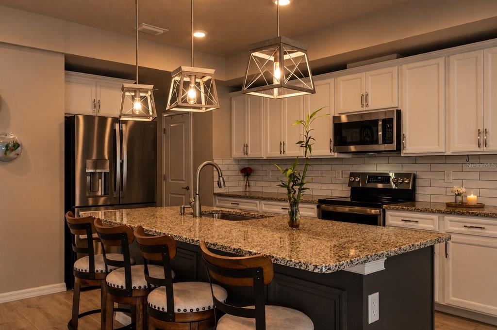A kitchen features a granite-topped island, dark cabinetry, white upper cabinets, and three pendant lights — 12182 PIONEER AVENUE, WEEKI WACHEE, FL