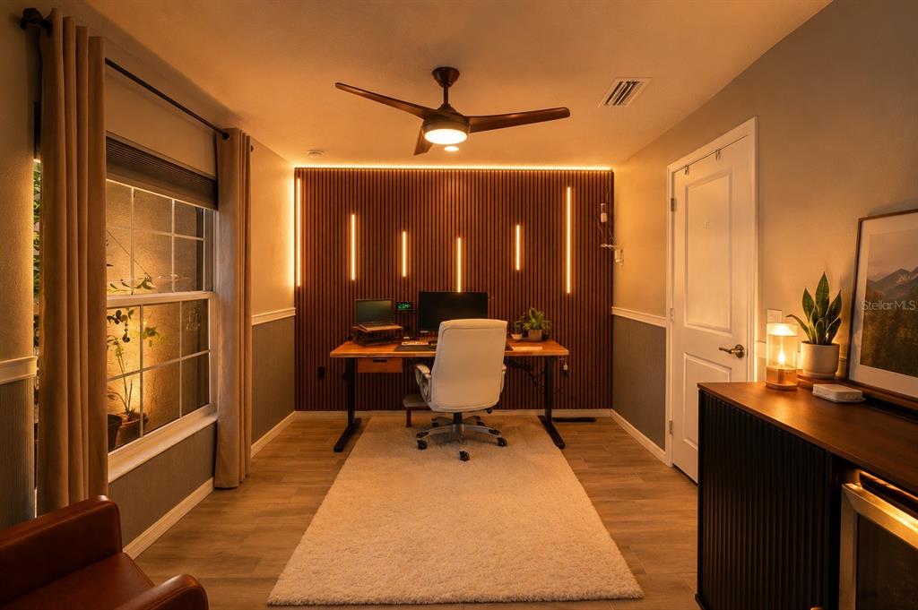 A home office features a wood-slat accent wall with integrated lighting, a desk, and rug — 12182 PIONEER AVENUE, WEEKI WACHEE, FL