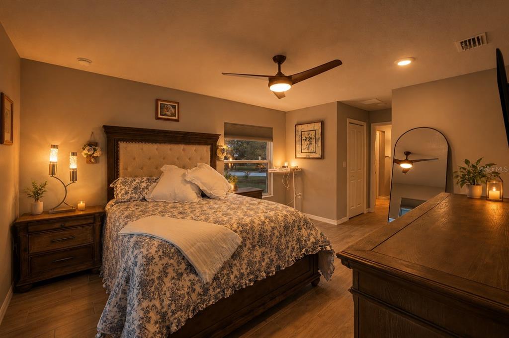 A bedroom features a tufted headboard, floral bedding, a ceiling fan, and a floor mirror — 12182 PIONEER AVENUE, WEEKI WACHEE, FL