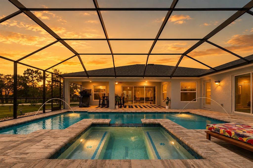 A swimming pool and spa are enclosed by a screened lanai at sunset — 12182 PIONEER AVENUE, WEEKI WACHEE, FL