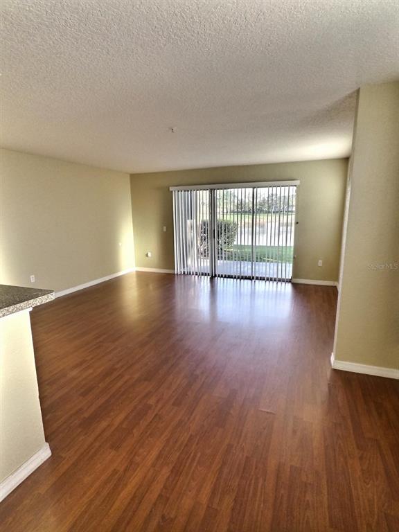 An empty living room features wood-look flooring, light-colored walls, and a sliding glass door — 13803 FAIRWAY ISLAND DRIVE UNIT 1618, ORLANDO, FL