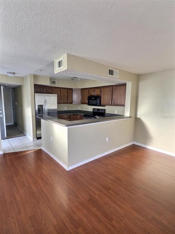 A kitchen with wood cabinets and stainless steel appliances overlooks a living area with flooring — 13803 FAIRWAY ISLAND DRIVE UNIT 1618, ORLANDO, FL