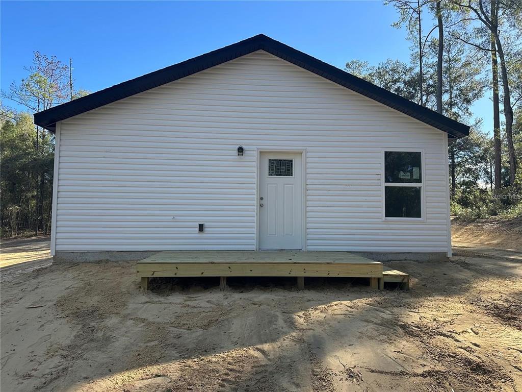 The exterior of a white-sided house features a wooden deck and a single door — 13725 SW 111TH LANE, DUNNELLON, FL