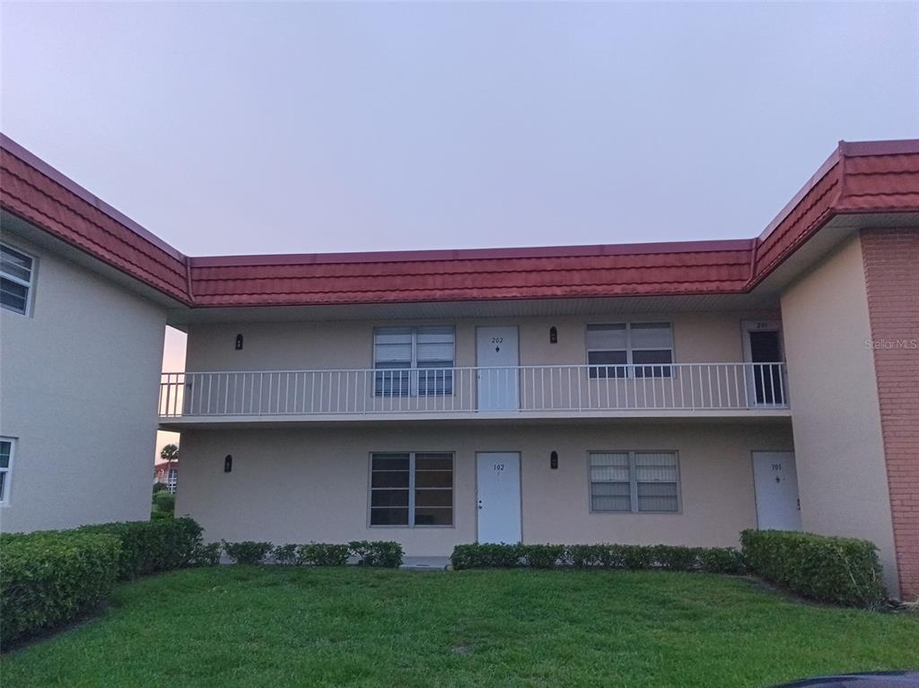 A two-story apartment building with a red roof, white railings, and beige exterior walls — 57 WOODLAND DRIVE UNIT 102, VERO BEACH, FL
