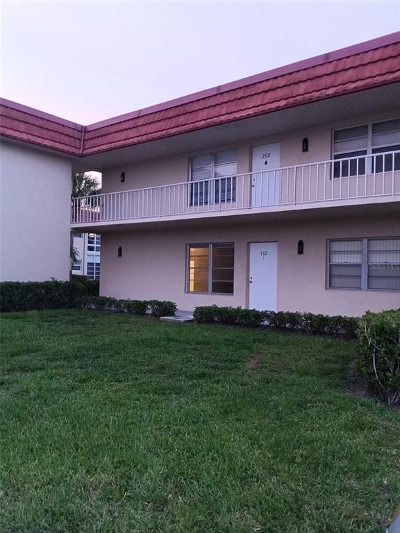 A two-story apartment building exterior features a white balcony, tan stucco walls, and red roof — 57 WOODLAND DRIVE UNIT 102, VERO BEACH, FL
