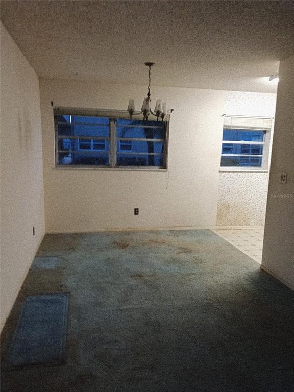 A dining room with a chandelier, blue carpet, and two windows overlooking an exterior building — 57 WOODLAND DRIVE UNIT 102, VERO BEACH, FL