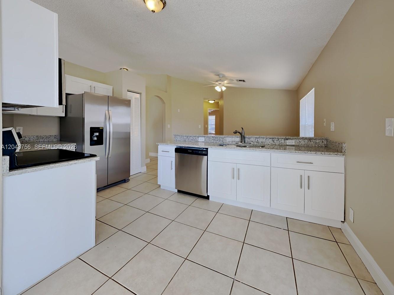 A kitchen features white cabinets, granite countertops, stainless steel appliances, and beige tile flooring — MIAMI, FL