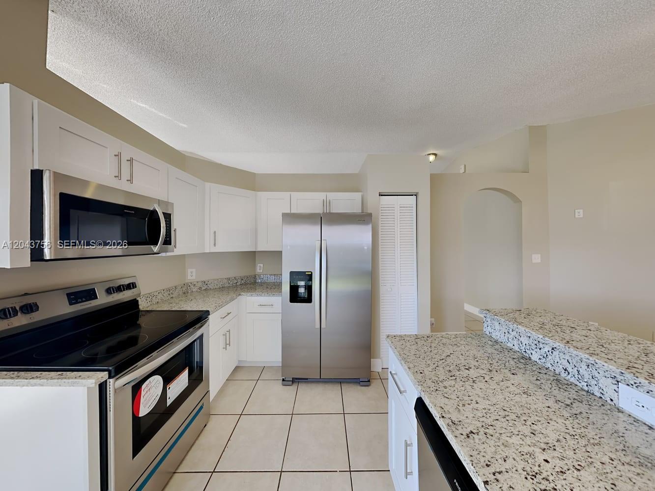 A kitchen features white cabinets, granite countertops, stainless steel appliances, and light tile flooring — MIAMI, FL