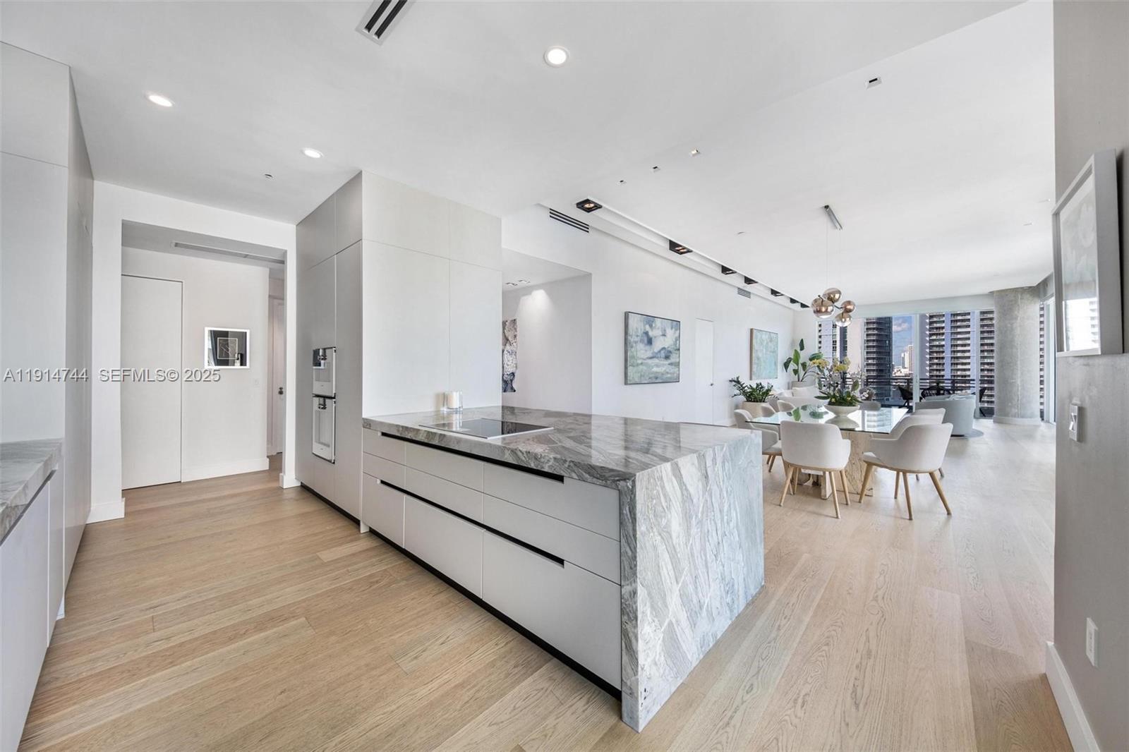 A modern kitchen features a marble waterfall island, light wood flooring, and an open layout — 900 Brickell Key Blvd # 1403, Miami FL 33131, MIAMI, FL