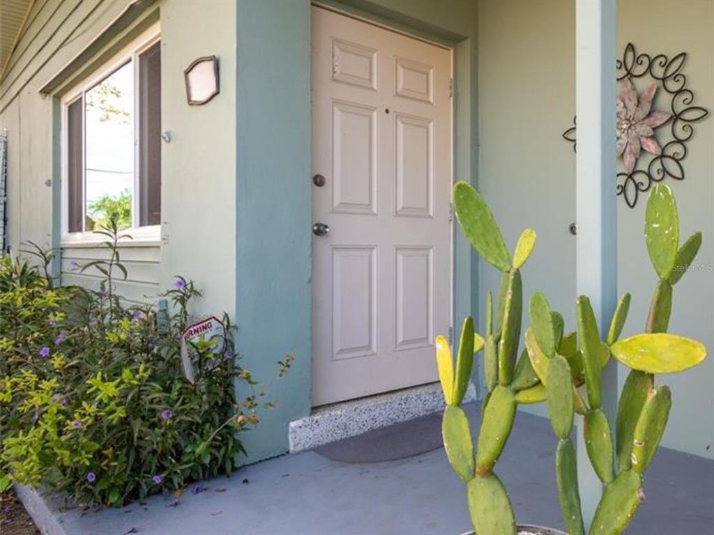 A light-colored front door is flanked by a window, a cactus, and a wall decoration — 2456 ELKCAM BOULEVARD, PORT CHARLOTTE, FL
