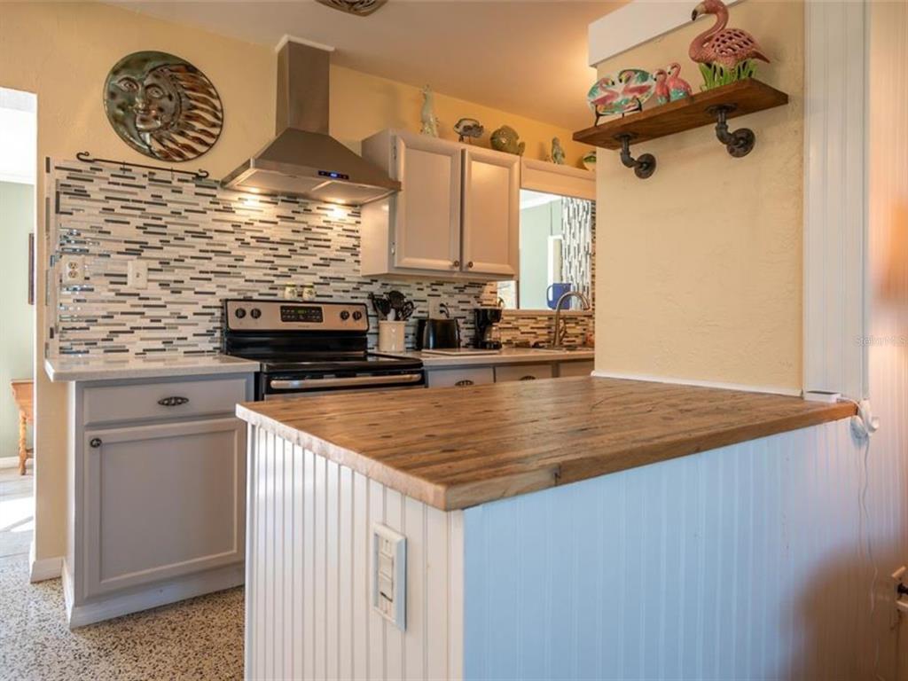 A kitchen features a wooden breakfast bar, light gray cabinets, and a tiled backsplash — 2456 ELKCAM BOULEVARD, PORT CHARLOTTE, FL