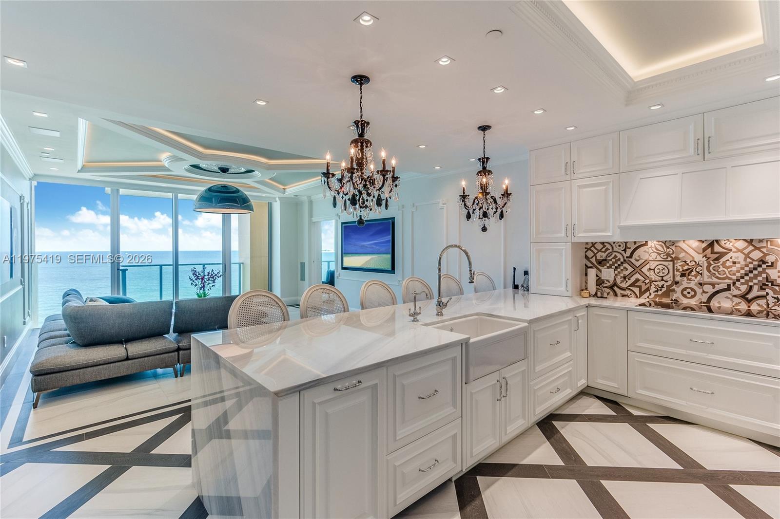 A modern white kitchen with a large island, crystal chandeliers, and an ocean view — 1455 Ocean Dr # 1607, Miami Beach FL 33139, MIAMI BEACH, FL