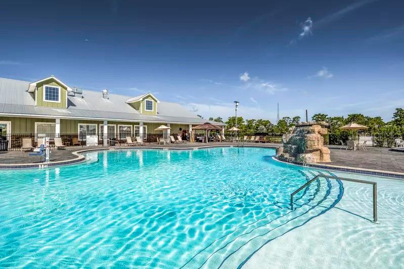 A swimming pool with a rock feature sits in front of a green community building — 0 HIGHWAY 630 E UNIT 313, LAKE WALES, FL