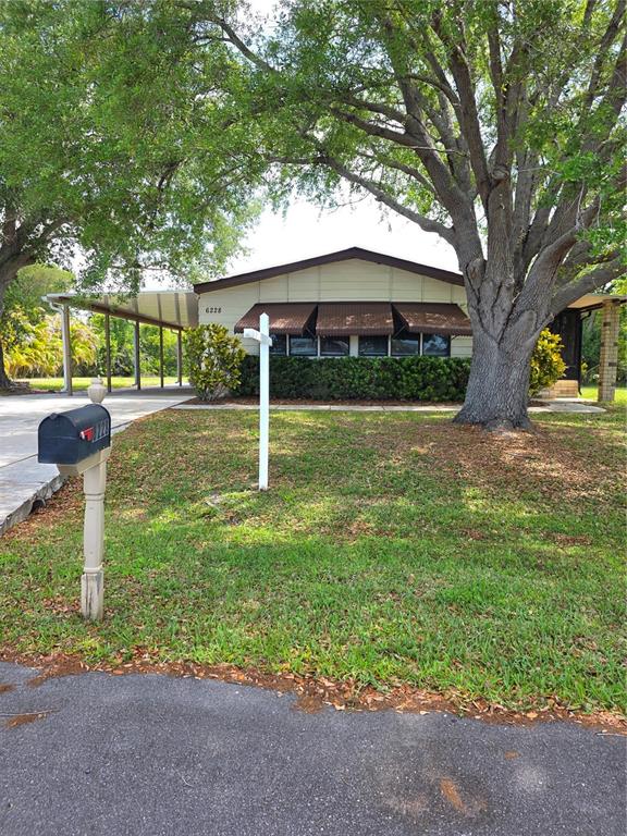 A single-story house with a carport and a large tree in the front yard — 6228 FALCON DRIVE, ENGLEWOOD, FL