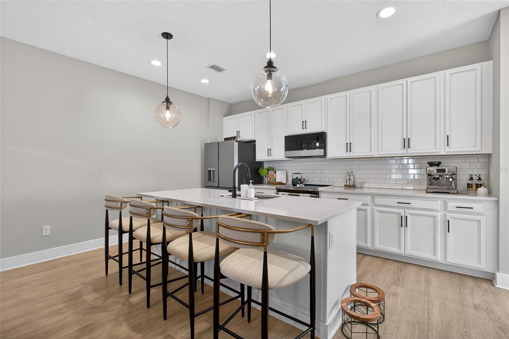 A kitchen features white cabinets, a quartz island with bar seating, and light wood flooring — 2526 13TH AVENUE N, ST PETERSBURG, FL