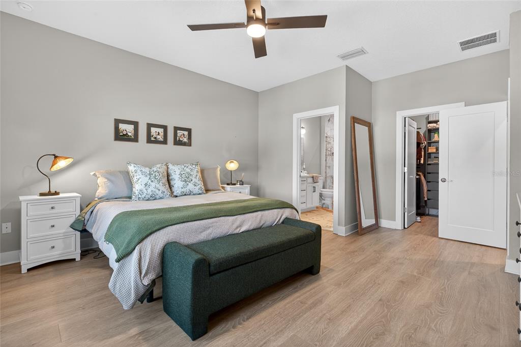 A bedroom features light wood floors, a bed with a green bench, and an attached bathroom — 2526 13TH AVENUE N, ST PETERSBURG, FL