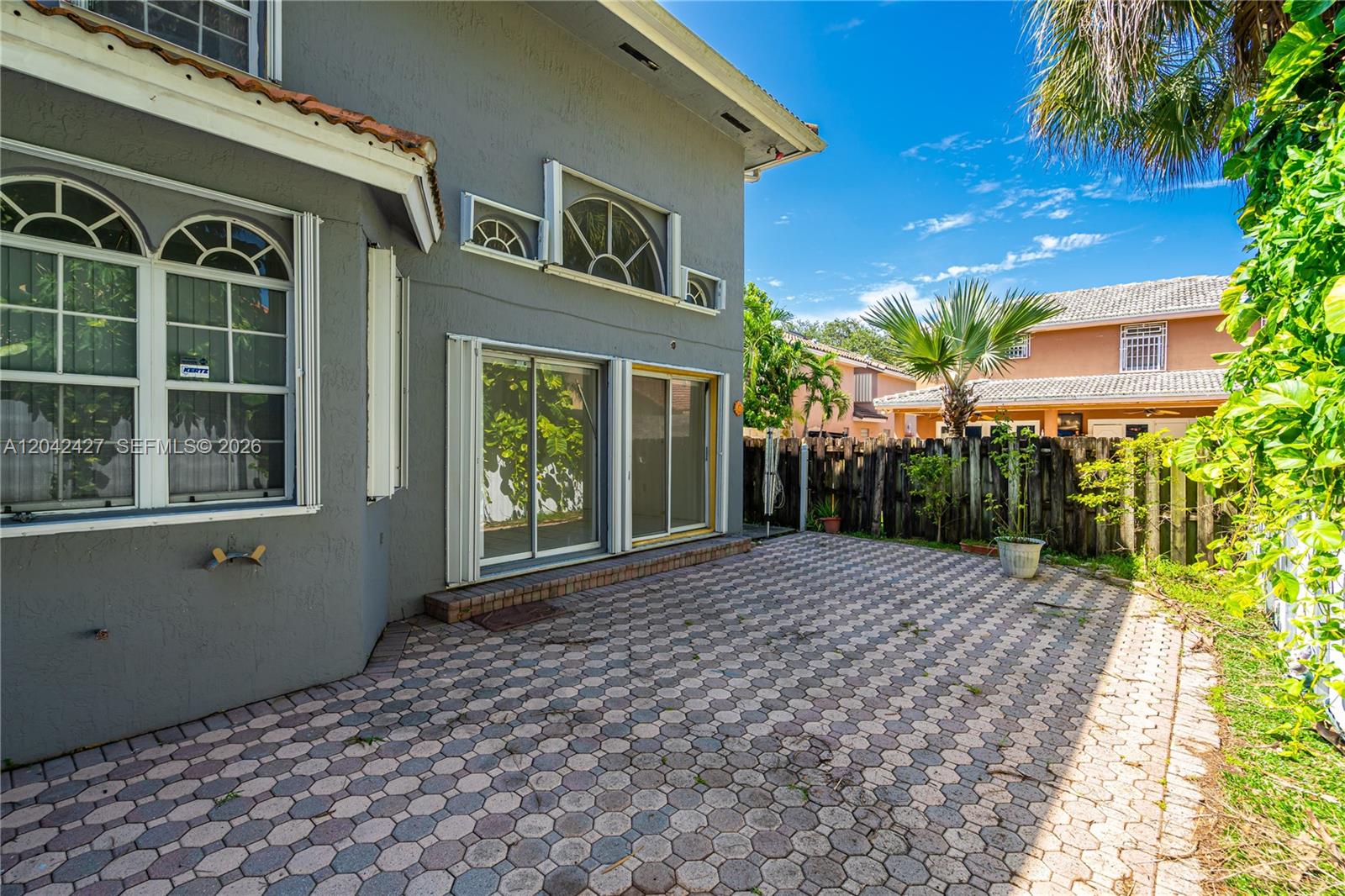 A gray house exterior features a paved patio, sliding glass doors, and arched windows — 15251 NW 89th Ave, Miami Lakes FL 33018, MIAMI LAKES, FL