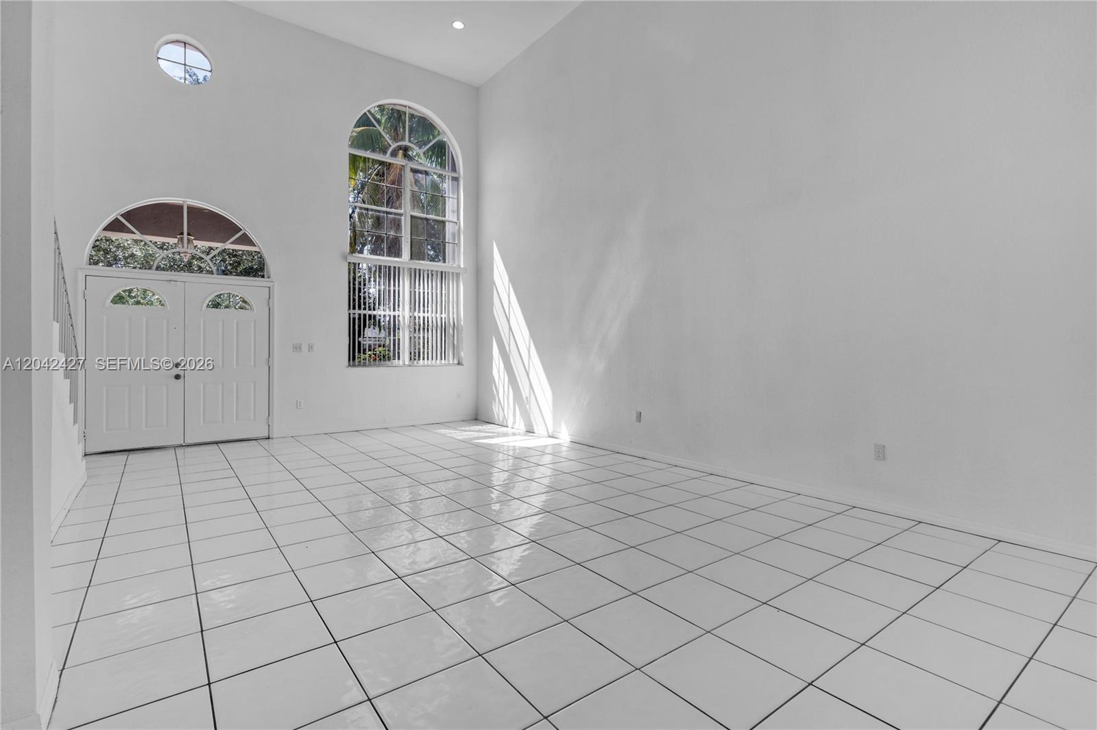 A bright, empty room features white tiled floors, high ceilings, and a large arched window — 15251 NW 89th Ave, Miami Lakes FL 33018, MIAMI LAKES, FL
