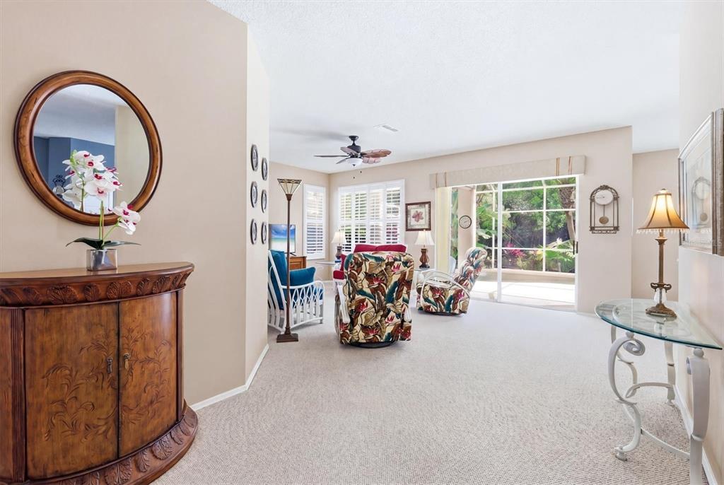 A carpeted living room features a wooden cabinet, floral armchairs, and sliding glass doors — 5159 51ST LANE W, BRADENTON, FL