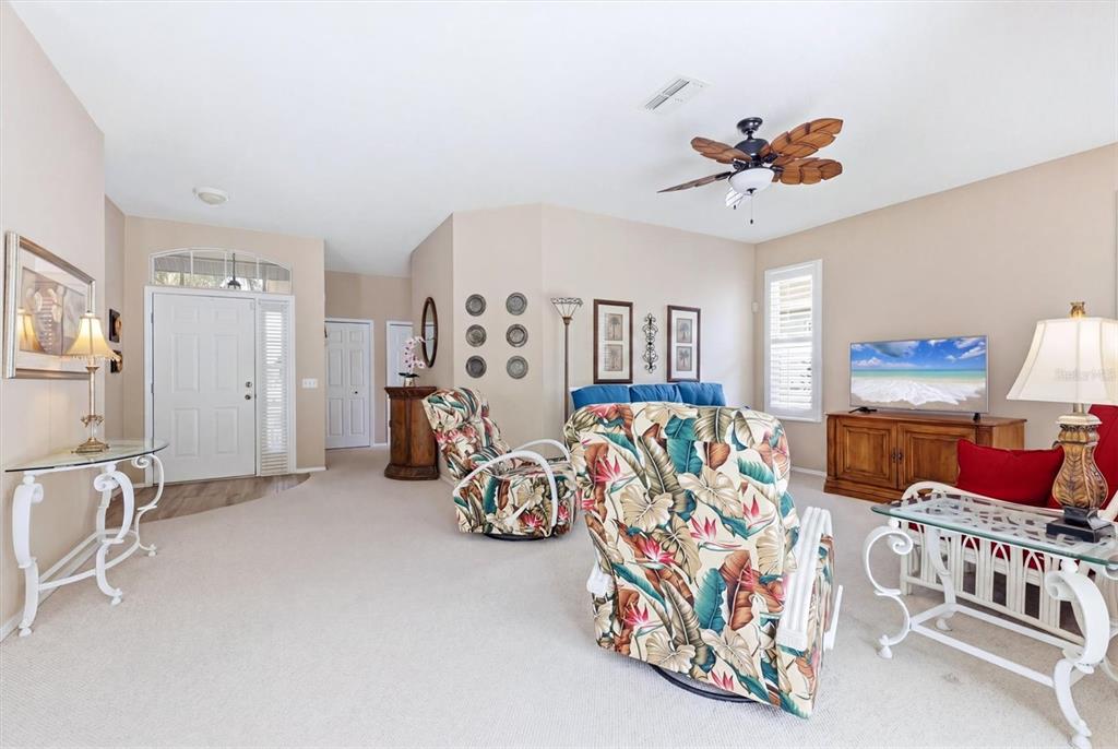 A living room features beige carpeting, a tropical-print armchair, and a ceiling fan — 5159 51ST LANE W, BRADENTON, FL