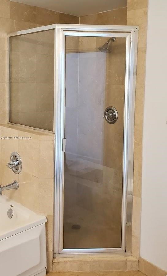 A corner glass shower stall with a silver frame sits next to a white bathtub — CORAL GABLES, FL