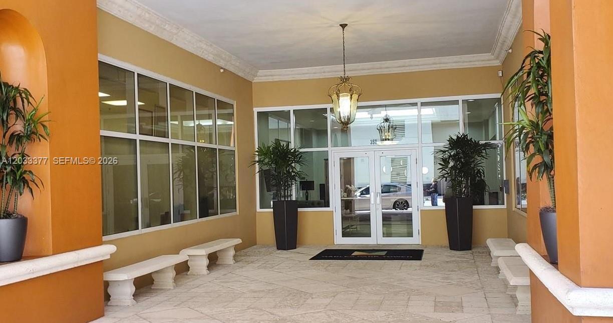 This is an outdoor covered building entrance with stone flooring, potted plants, and benches — CORAL GABLES, FL
