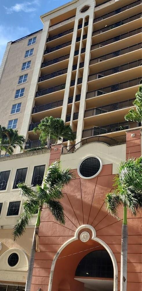 A low-angle view of a multi-story apartment building with balconies and a decorative arched entrance — CORAL GABLES, FL